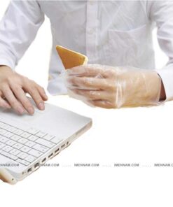 فردی در حال کار کردن با لپ تاپ که دستکش پلاستیکی پوشیده و کیک در دستش