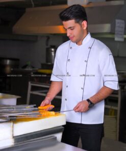 جوانی با لباس سرآشپز شایان سفید در داخل آشپزخانه یک چاقو و یک سیخ جوجه در دستانش